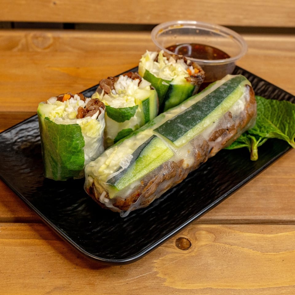 Vietnamese spring rolls with beef, lettuce, and cucumber, served with dipping sauce on a black plate.