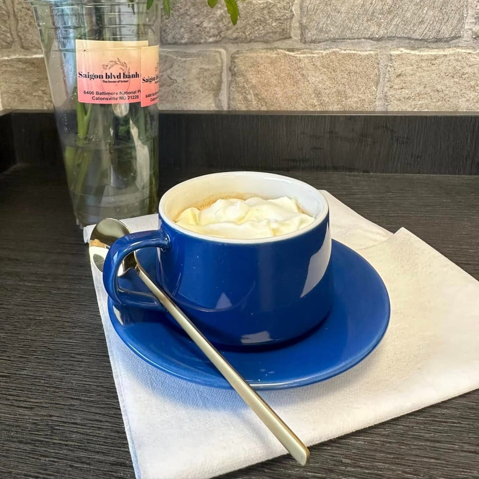 A blue cup of Vietnamese coffee with whipped cream and a spoon on a white napkin.